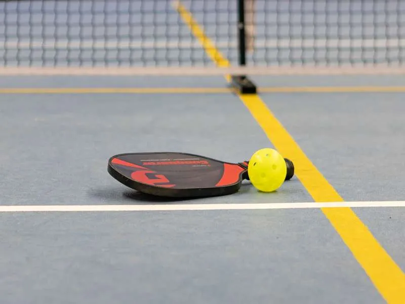 a pickleball racket and a yellow ball placed on the floor
