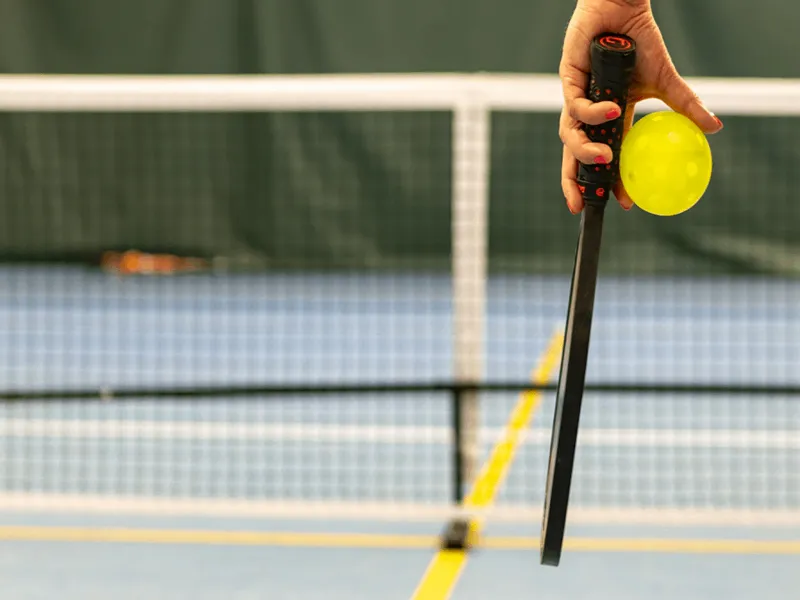 closeup picture of a hand holding pickleball paddle and yellow ball