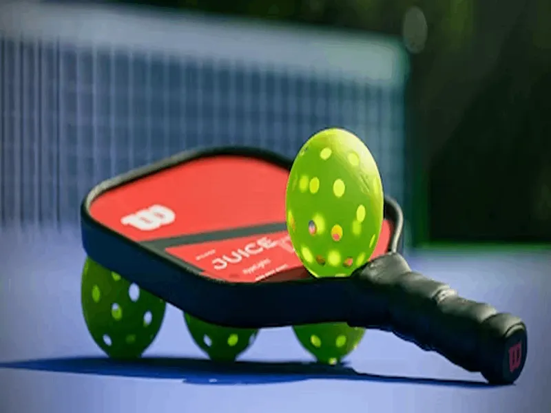 an image of red pickleball paddle placed on the floor along with four yellow wiffle balls