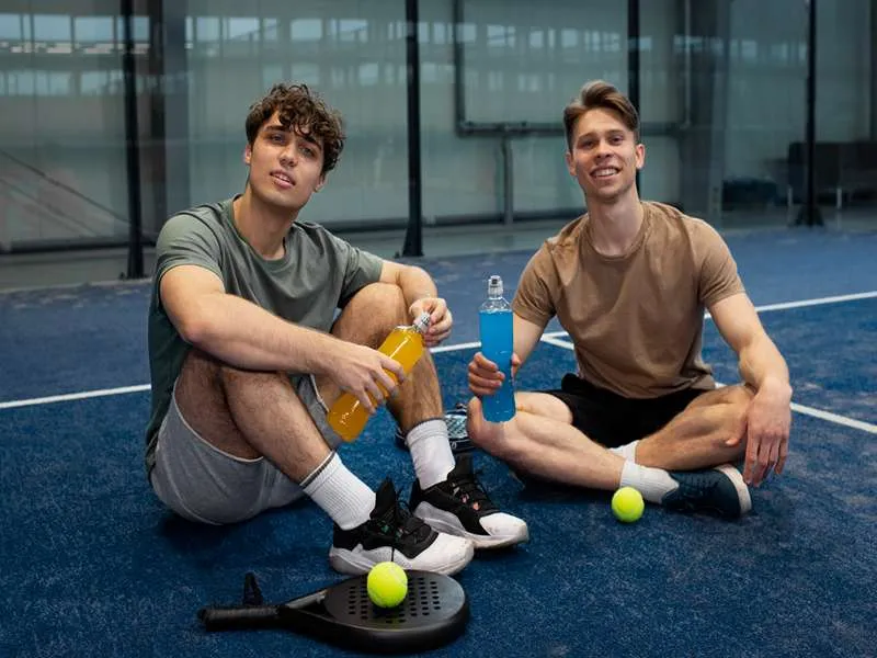 Two men looking at the camera with pickleball paddles and balls placed in front of them, discussing pickleball doubles strategies.