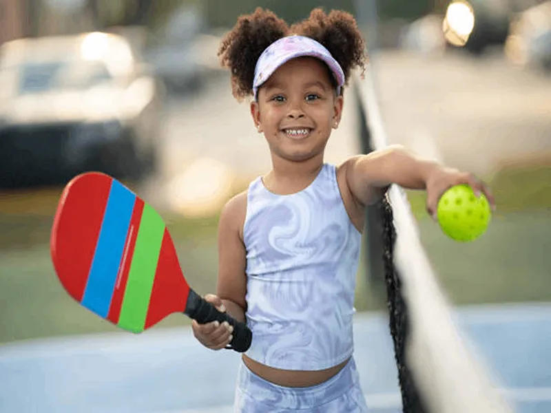 an image of a Hispanic girl holding a pickleball paddle and ball while standing on the pickleball court.