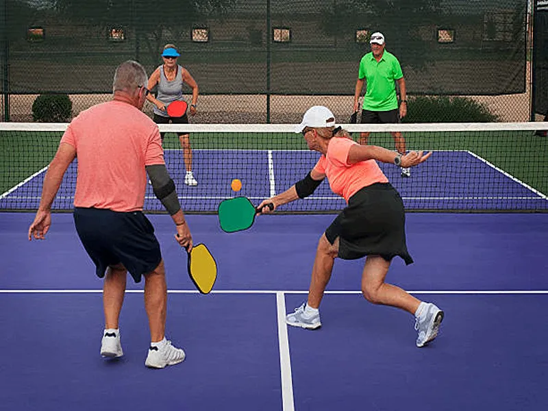 2 elderly couples can be seen playing a game of pickleball